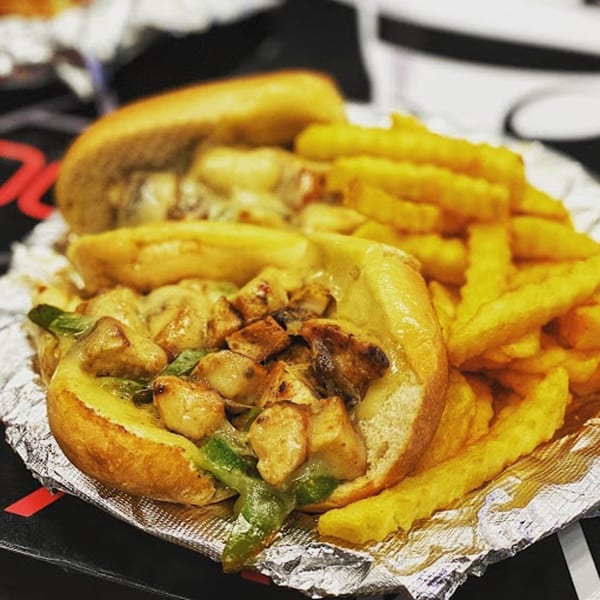 Two chicken and cheese subs with green peppers and a side of golden french fries on foil.