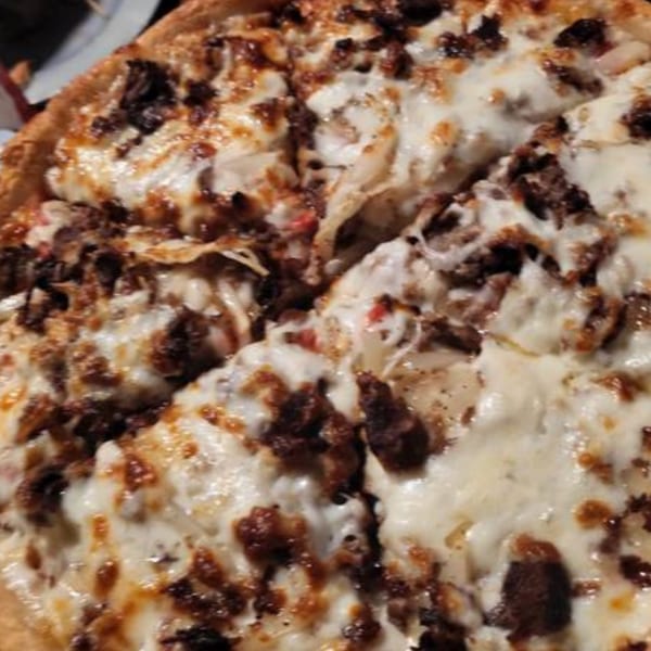 Close-up of a Goodfellas Pizza and Wings pizza, topped with melted cheese and dark meat.