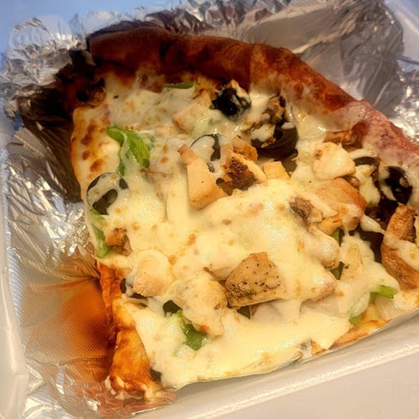 A slice of Goodfellas Pizza with chicken, olives, and green peppers, served in foil.