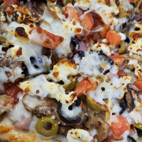 Close-up of a Goodfellas Pizza and Wings pizza with melted cheese, tomatoes, olives, and mushrooms.