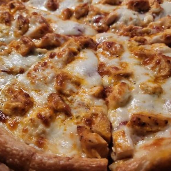 Close-up of a Goodfellas Pizza and Wings pizza, topped with melted cheese and chicken pieces.