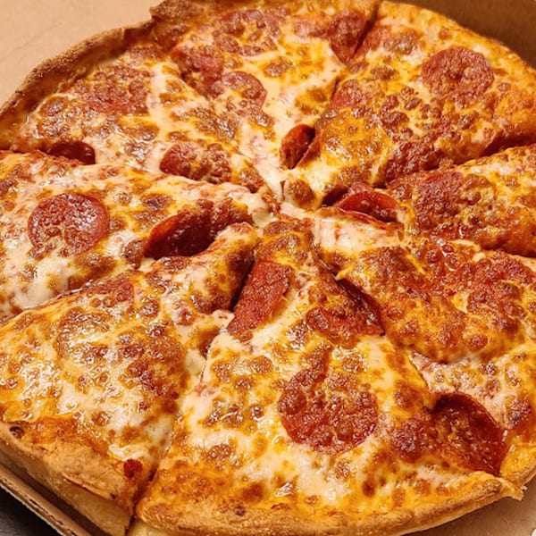 A close-up of a Goodfellas Pizza and Wings pepperoni pizza, cut into slices, in a cardboard box.